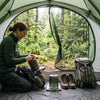 A camper organizing gear inside a tent vestibule with forest views through the mesh door