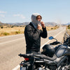 A motorcyclist pulling on a thin cooling balaclava before putting on a helmet on a summer road