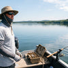 An angler on a boat deck fully geared with wide-brim hat, sunglasses, gaiter and sun sleeves