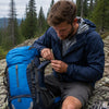 Hiker field-repairing the strap of a Finvizo 55L backpack with a sewing kit on a trail