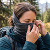A person adjusting a neck gaiter snugly over the nose and ears for a secure fit