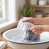 Hands gently hand-washing sun-protective sleeves in a basin of soapy water