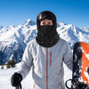 Skier in a black balaclava ski mask with goggles on a sunny groomed slope at a mountain resort