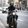 Motorcyclist wearing a black balaclava under a full-face helmet riding through city streets