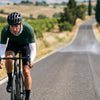 A road cyclist riding on a sunny country road wearing sun sleeves and a neck gaiter