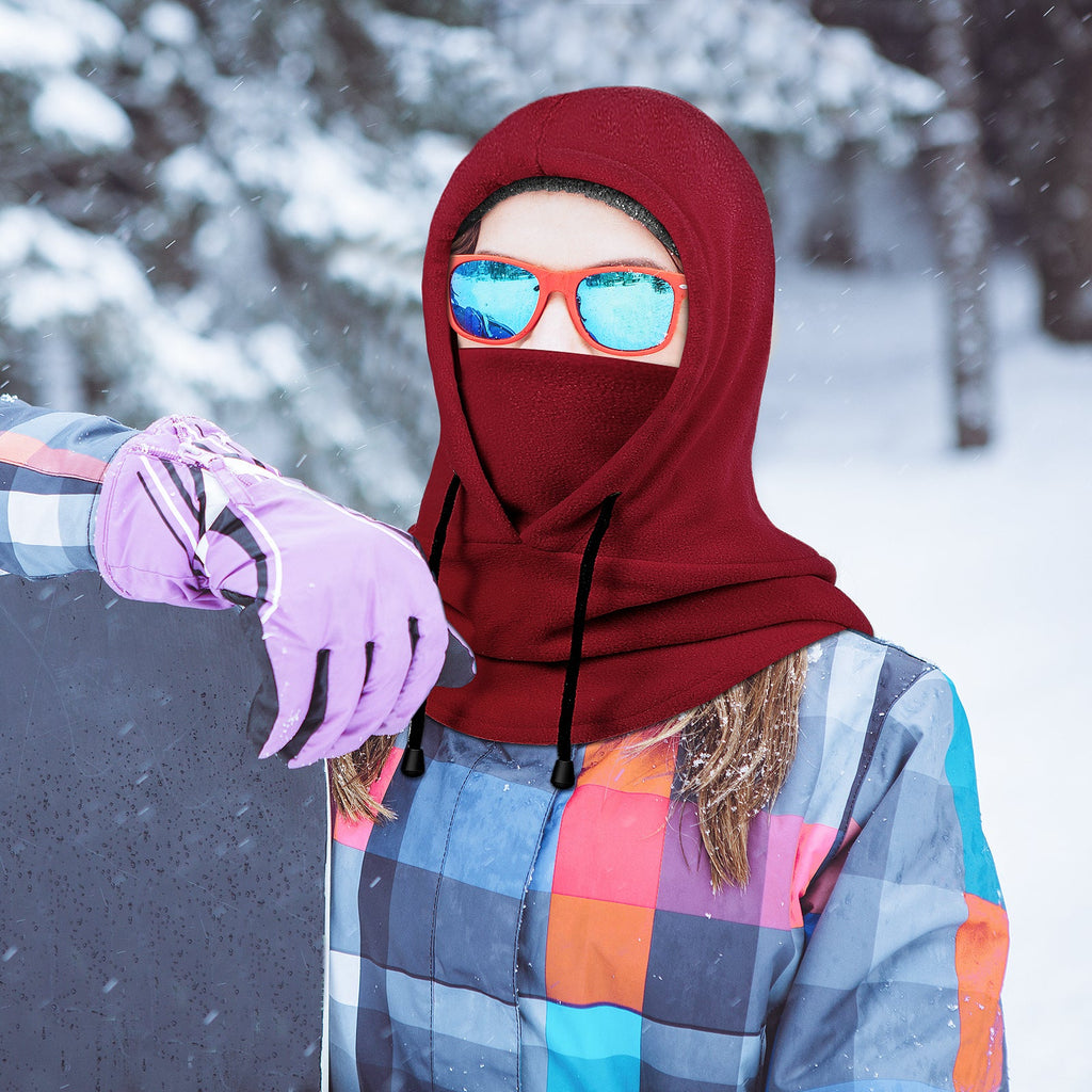 Woman wearing a red fleece balaclava holding a snowboard on a snowy mountain