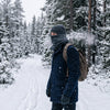 A person walking through a snowy pine forest wearing a thick fleece neck warmer