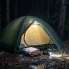 A tent glowing from a headlamp inside during a stormy night with an emergency blanket at the entrance