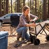 A person unfolding a collapsible four-wheel wagon cart at a campsite