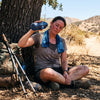 An exhausted hiker resting in trail-side shade with a wet cooling towel on the neck