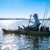 A kayak angler on bright open water wearing a neck gaiter, sun sleeves and wide-brim hat