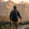 Hiker wearing a black 45L backpack with trekking poles on a rocky mountain trail at golden hour