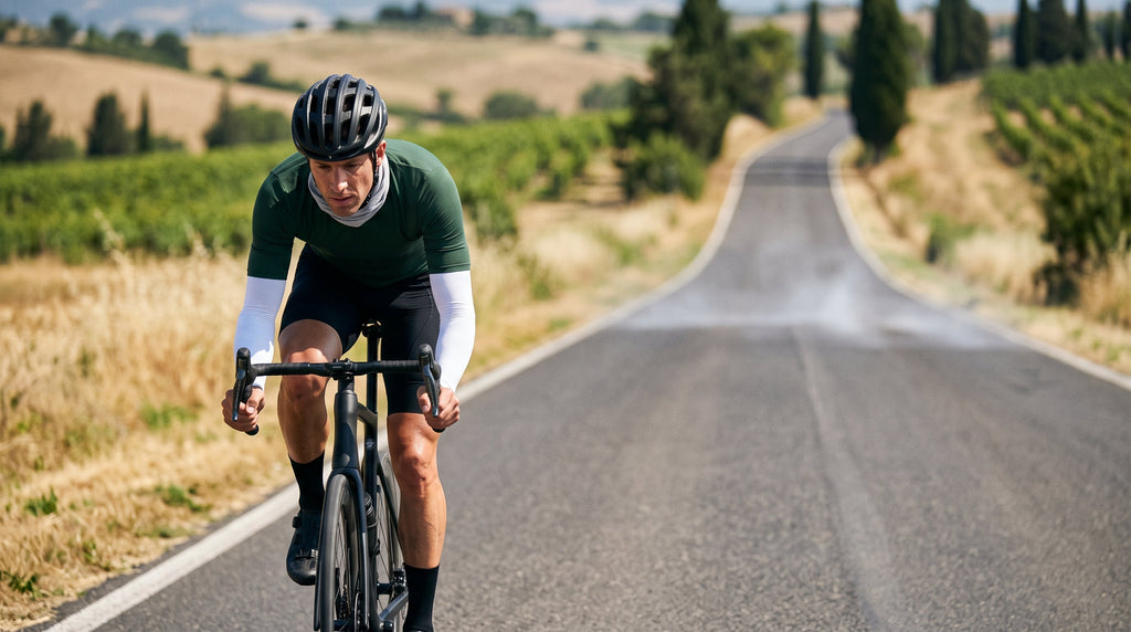 A road cyclist riding on a sunny country road wearing sun sleeves and a neck gaiter