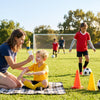 Kids at sunny soccer practice with one child wearing sun sleeves and a parent applying sunscreen