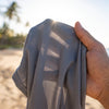 A hand holding sun-protective fabric up to bright sunlight to show how the weave blocks rays